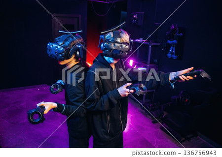 Doing hands gestures. Two young men in virtual reality glasses indoors Doing hands gestures. Two young men in virtual reality glasses indoors 136756943
