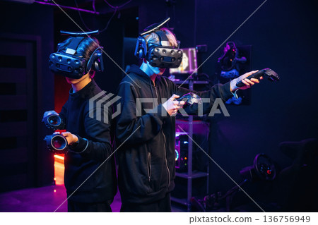 In the dark room. Two young men in virtual reality glasses indoors In the dark room. Two young men in virtual reality glasses indoors 136756949
