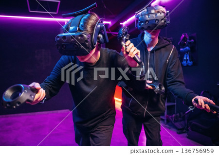 Conception of teamplay. Two young men in virtual reality glasses indoors Conception of teamplay. Two young men in virtual reality glasses indoors 136756959