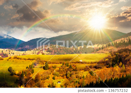 autumn landscape of rural region in mountains at sunset. rolling hills with green alps in dappled evening light. serene countryside under cloudy sky. timeless nostalgia book cover with rainbow 136757232