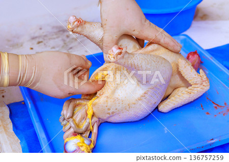 Butcher with gloves works on raw chicken on blue cutting board in kitchen. 136757259