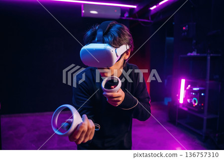 Action game experience. Young man is in virtual reality glasses indoors Action game experience. Young man is in virtual reality glasses indoors 136757310