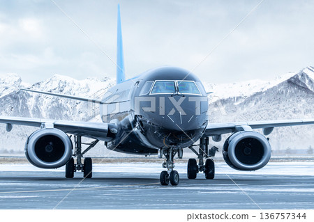 Close-up front view of a black passenger aircraft taxiing at winter airport on the background of high snow capped mountains 136757344
