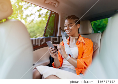 Young black woman sitting on back seat in car and using smartphone 136757452