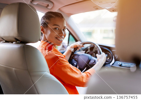 Black woman turning back from driver seat and smiling warmly at passenger Black woman turning back from driver seat and smiling warmly at passenger 136757455