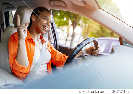 Young black woman driving car raising index finger with cheerful expression 136757462