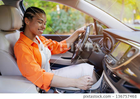 Smiling young black woman adjusting gear shift while driving modern car Smiling young black woman adjusting gear shift while driving modern car 136757468