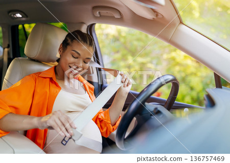 Smiling young black pregnant woman fastening seatbelt inside car Smiling young black pregnant woman fastening seatbelt inside car 136757469