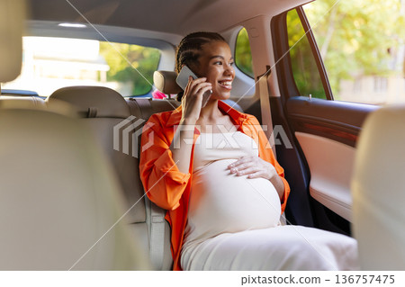 Smiling young black pregnant woman sitting in back seat talking on phone 136757475