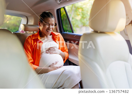 Young black pregnant woman in back car seat holding belly in pain 136757482
