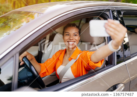 Young black woman taking selfie inside car while driving, capturing joyful moment 136757487