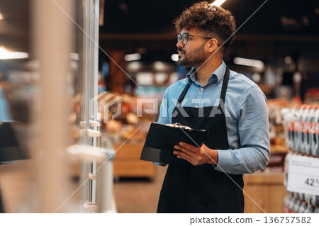 With notepad. Male worker is in the grocery store With notepad. Male worker is in the grocery store 136757582