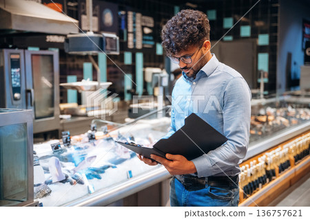 Black notepad in hands. Male worker is in the grocery store 136757621