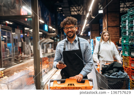 Phone in hands, standing. Male worker is in the grocery store 136757629
