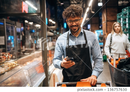 Phone in hands, standing. Male worker is in the grocery store Phone in hands, standing. Male worker is in the grocery store 136757630