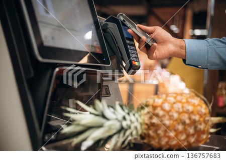 With pineapple. Close up view of man customer that is paying for products by credit card in grocery store 136757683