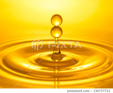 Golden Water Drop Collision Creating Ripple Splash on Yellow Background 136757722