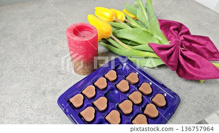 Heart shaped chocolate candy in plastic box with tulip bouquet and candle on table. Romantic gift and celebration concept Heart shaped chocolate candy in plastic box with tulip bouquet and candle on table. Romantic gift and celebration concept 136757964