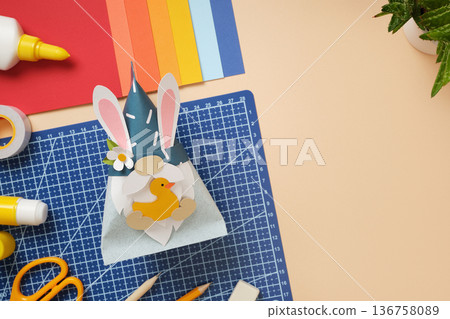 DIY Easter gnome with bunny ears and paper duck on blue background. Cutting mat, scissors, and colorful paper. Copyspace DIY Easter gnome with bunny ears and paper duck on blue background. Cutting mat, scissors, and colorful paper. Copyspace 136758089
