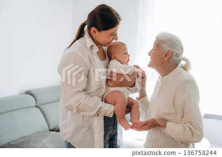 Enjoying of being together. Mother, grandmother and little baby child on hands indoors Enjoying of being together. Mother, grandmother and little baby child on hands indoors 136758244