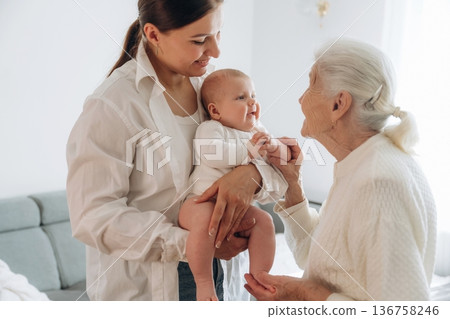Enjoying of being together. Mother, grandmother and little baby child on hands indoors Enjoying of being together. Mother, grandmother and little baby child on hands indoors 136758246