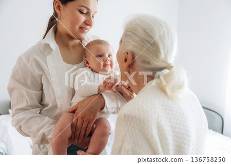 Standing, looking at each other. Mother, grandmother and little baby child on hands indoors 136758250