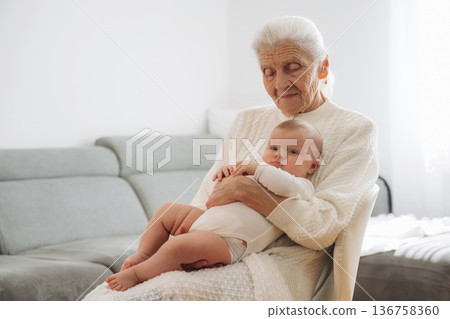 Holding toddler in hands. Grandmother with cute toddler baby at home Holding toddler in hands. Grandmother with cute toddler baby at home 136758360