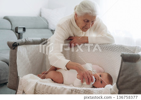 Feeding with a bottle. Grandmother with cute toddler baby at home Feeding with a bottle. Grandmother with cute toddler baby at home 136758377