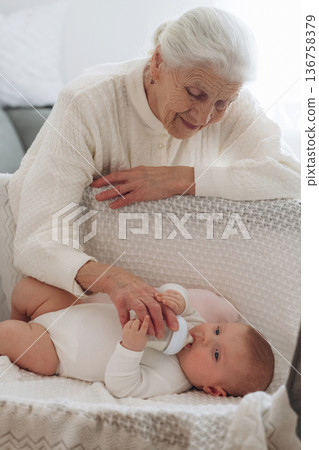 Feeding with a bottle. Grandmother with cute toddler baby at home Feeding with a bottle. Grandmother with cute toddler baby at home 136758379