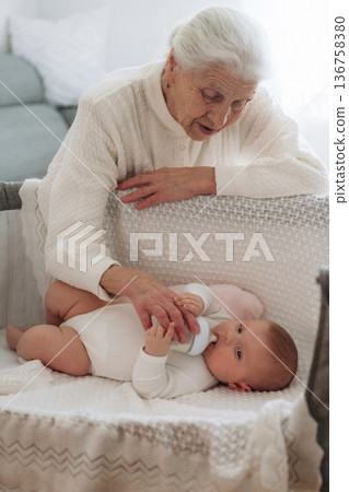 Feeding with a bottle. Grandmother with cute toddler baby at home Feeding with a bottle. Grandmother with cute toddler baby at home 136758380
