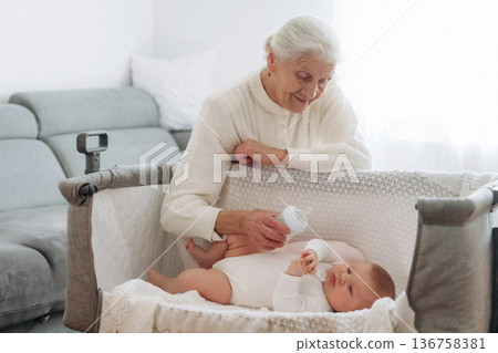 Feeding with a bottle. Grandmother with cute toddler baby at home Feeding with a bottle. Grandmother with cute toddler baby at home 136758381