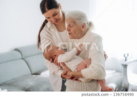 Cheerful facial expression. Mother, grandmother and little baby child on hands indoors 136758490