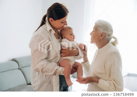Enjoying of being together. Mother, grandmother and little baby child on hands indoors 136758499