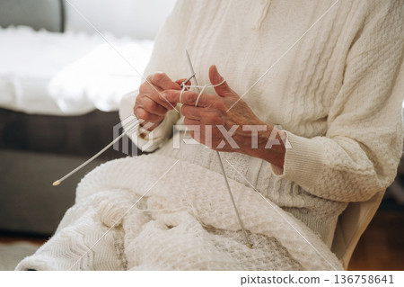 Close up view of grandma that sits in a chair at home and knits Close up view of grandma that sits in a chair at home and knits 136758641