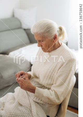 Grandma sits in a chair at home and knits clothes 136758642