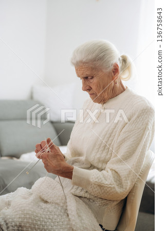 Grandma sits in a chair at home and knits clothes Grandma sits in a chair at home and knits clothes 136758643