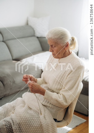 Grandma sits in a chair at home and knits clothes Grandma sits in a chair at home and knits clothes 136758644