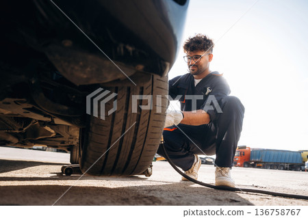 Sitting, side view, changing tire, using screwdriver. Mechanic is with the car outdoors 136758767