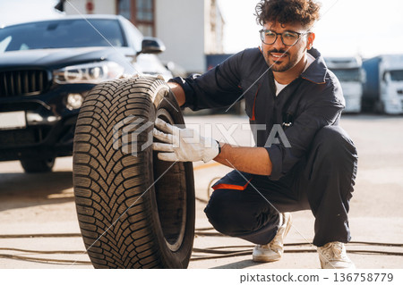 Looking forward, with tire. Mechanic is with the car outdoors Looking forward, with tire. Mechanic is with the car outdoors 136758779