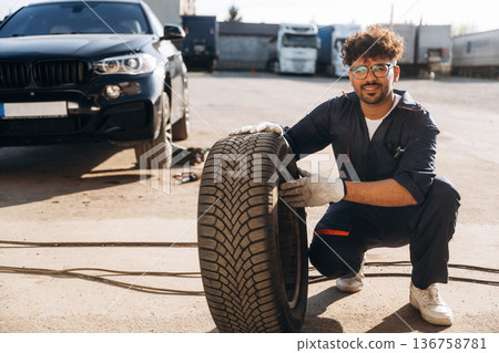 Looking forward, with tire. Mechanic is with the car outdoors Looking forward, with tire. Mechanic is with the car outdoors 136758781