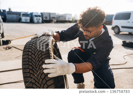 Checking the tire. Mechanic is with the car outdoors Checking the tire. Mechanic is with the car outdoors 136758783