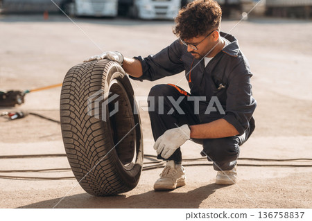 Sitting, in white gloves. Man mechanic is with new tire Sitting, in white gloves. Man mechanic is with new tire 136758837