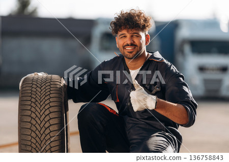 Sitting, in white gloves. Man mechanic is with new tire 136758843