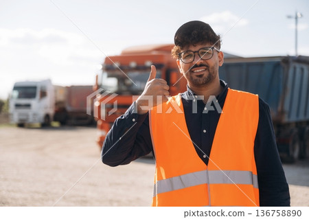 In orange uniform. Male worker is near truck outdoors In orange uniform. Male worker is near truck outdoors 136758890