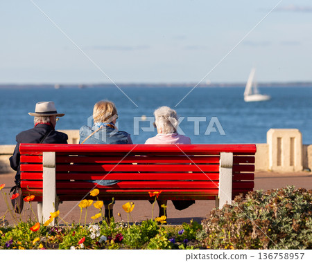 people sitting on a bench looking at the sea 136758957