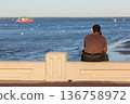 people sitting on a bench looking at the sea 136758972