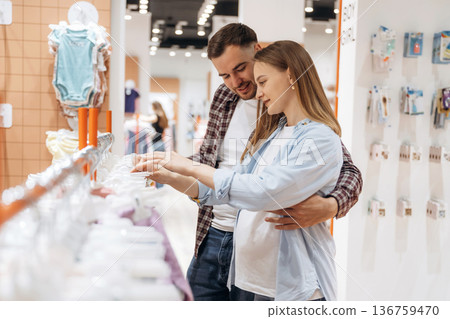 Feeling good, choosing the wear. Pregnant woman with man are in the kid's clothing store 136759470