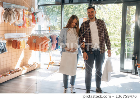 Pregnant woman with man are in the kid's clothing store 136759476
