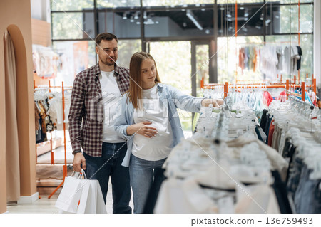 Side view, wear is hanging. Pregnant woman with man are in the kid's clothing store 136759493
