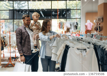 Holding boy in hands. Father, son and pregnant mother are in kid's clothing store Holding boy in hands. Father, son and pregnant mother are in kid's clothing store 136759506
